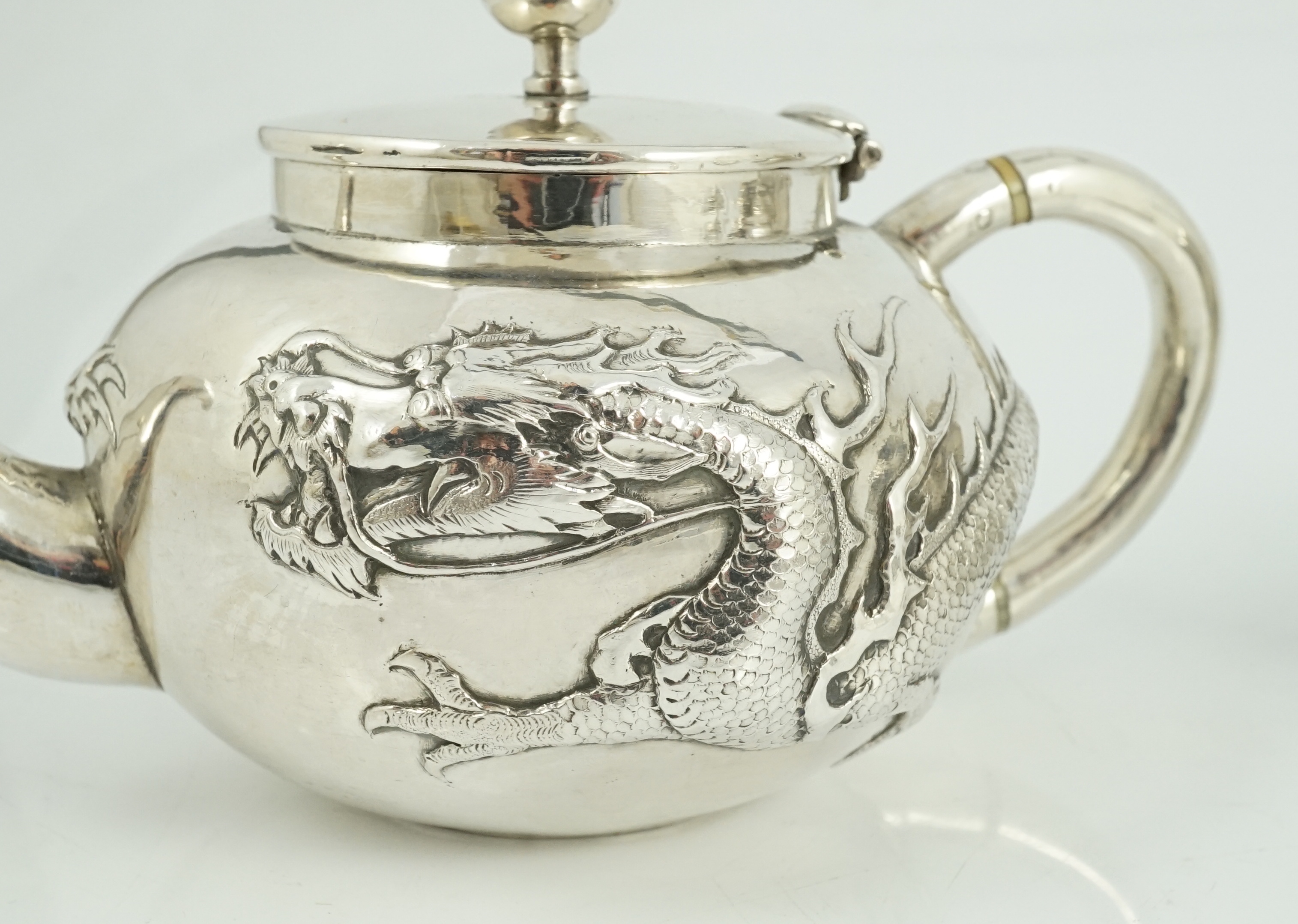 A Chinese three piece silver bachelor's tea set, by TC, decorated with dragon and one other similar Chinese silver two handled sugar bowl and cover, maker Sing Fat? and an odd cover